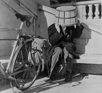a man seated, with a basket over his head